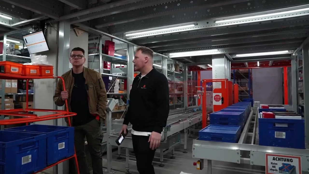 Igor Welder und ein Mitarbeiter der BRILLGRUPPE im Gespräch zwischen Kommissionierwagen und Förderanlage
