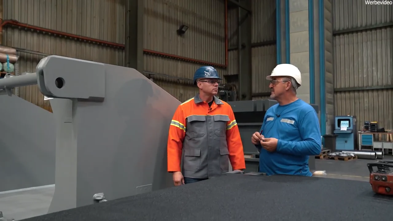 Igor Welder im Gespräch mit einem JEBENS-Mitarbeiter neben einer großen Stahlbaugruppe in der Fertigung